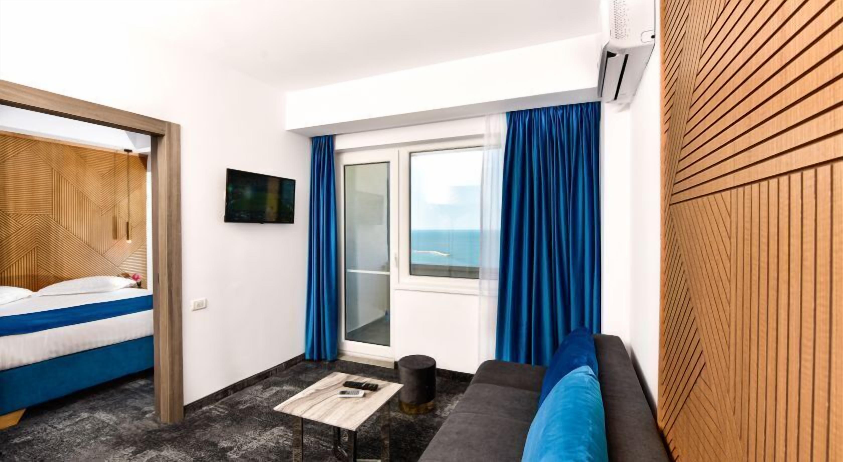 A hotel room with a bed, a sofa, a TV, and a window with curtains.