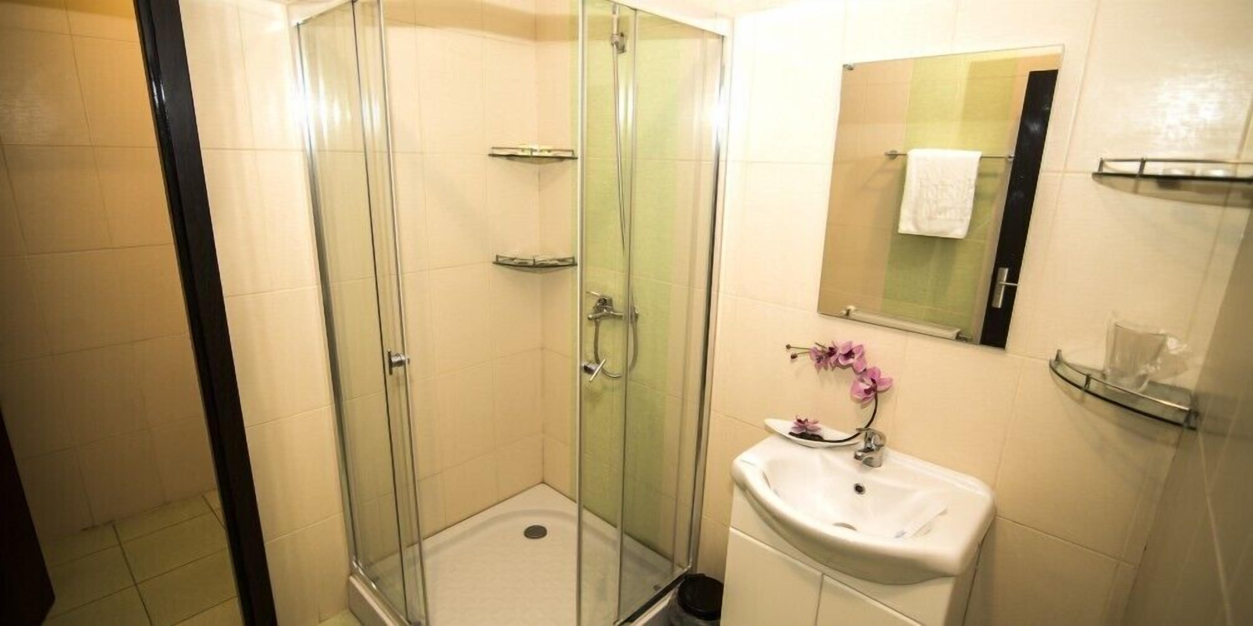 Un baño con ducha envuelta en vidrio, un lavamanos con espejo y un perchero para toallas.