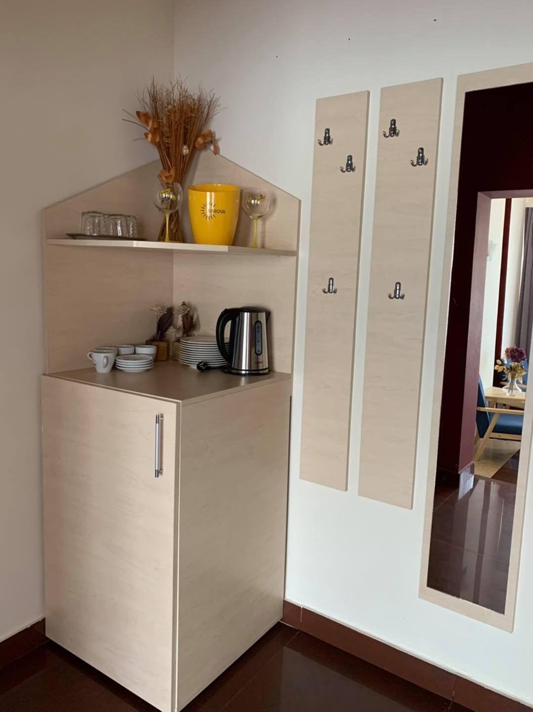 Una kitchenette compacta con refrigerador integrado, un estante pequeño con utensilios de cocina y un gabinete de pared con ganchos.