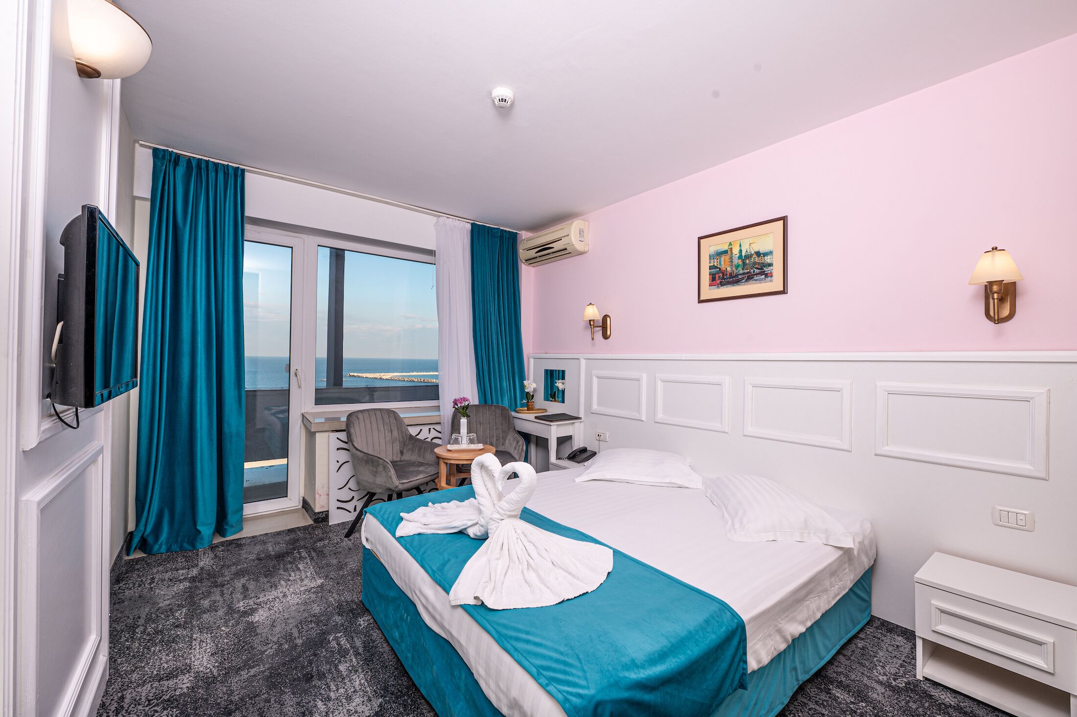 Habitación de hotel con cama, escritorio, silla, televisor y vistas a la ciudad.