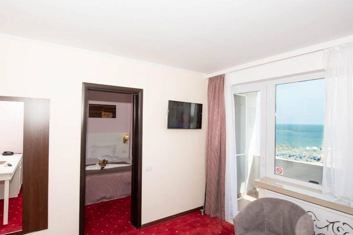 Et hotelværelse med seng, skrivebord, fjernsyn og et vindue med udsigt til havet.