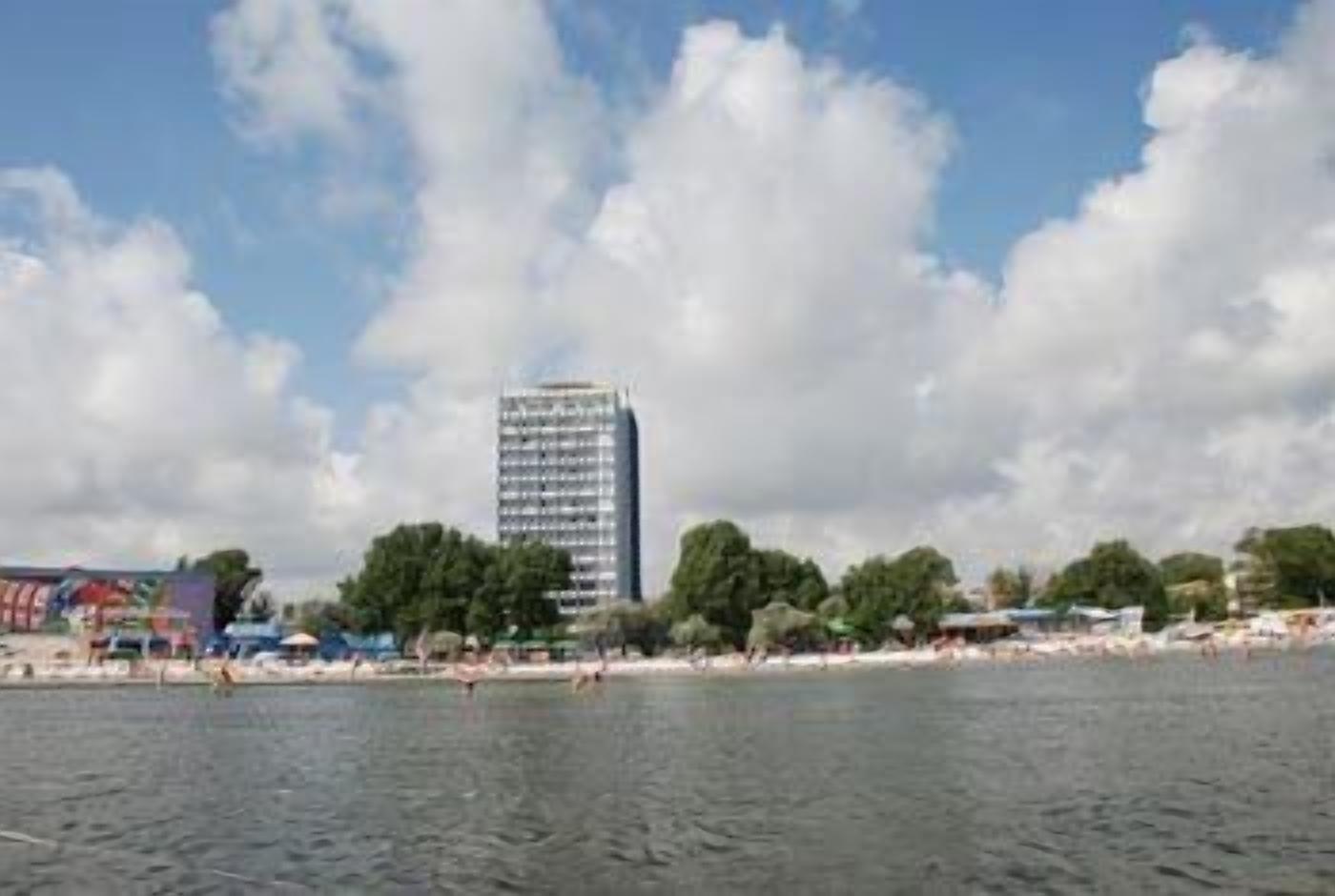 Vista al agua con un edificio alto, árboles y una zona de playa.