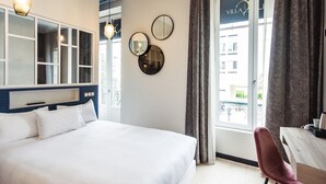 A hotel room with a large bed, a desk, and a view of the city through the window.