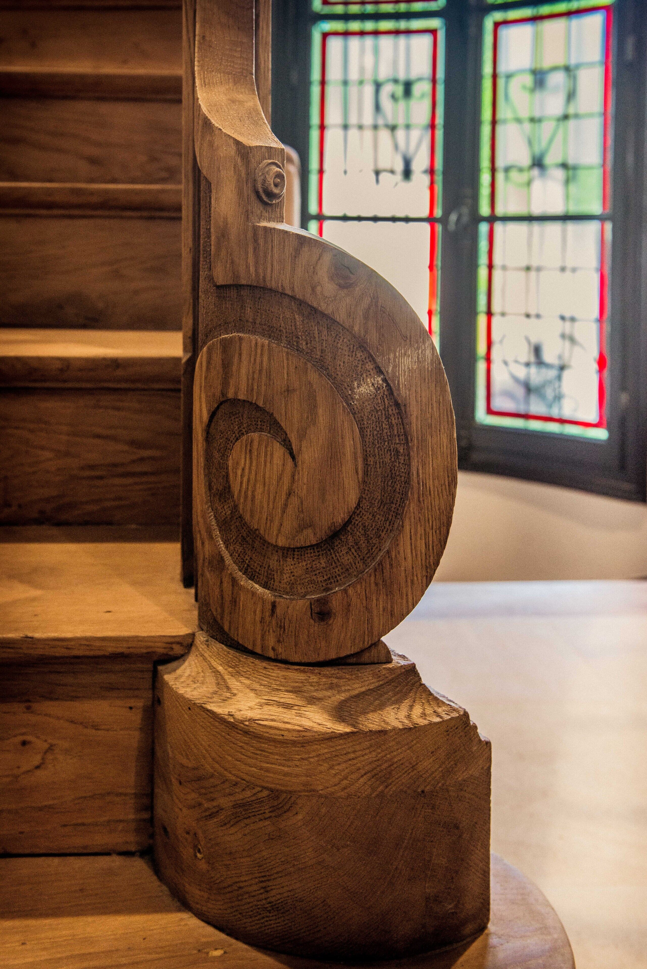 Una escalera en espiral de madera con un diseño rústico, frente a vidrieras de colores.