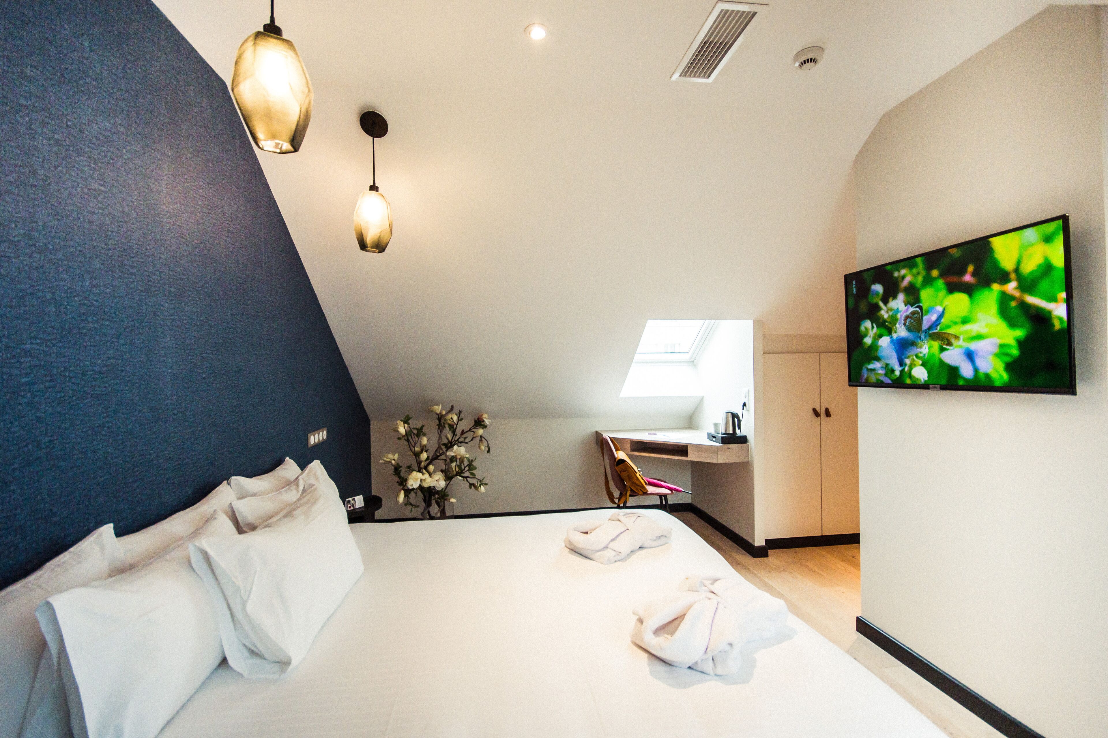 A modern hotel room with a bed, a desk, a TV, and a skylight.