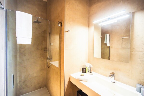 Un baño con ducha envuelta en vidrio, un lavamanos blanco y un espejo sobre él.