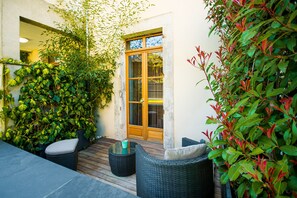 Un patio con mobiliario de mimbre, una terraza de madera y un ventanal que da a un espacio interior.
