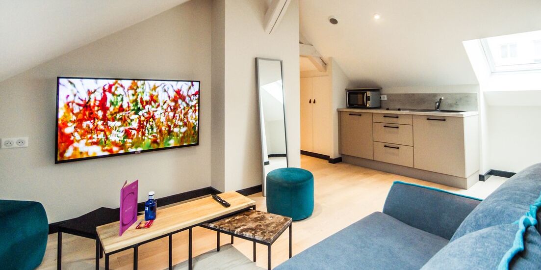 Un salon moderne avec une grande télévision, un canapé, une table basse et une cuisine en arrière-plan.