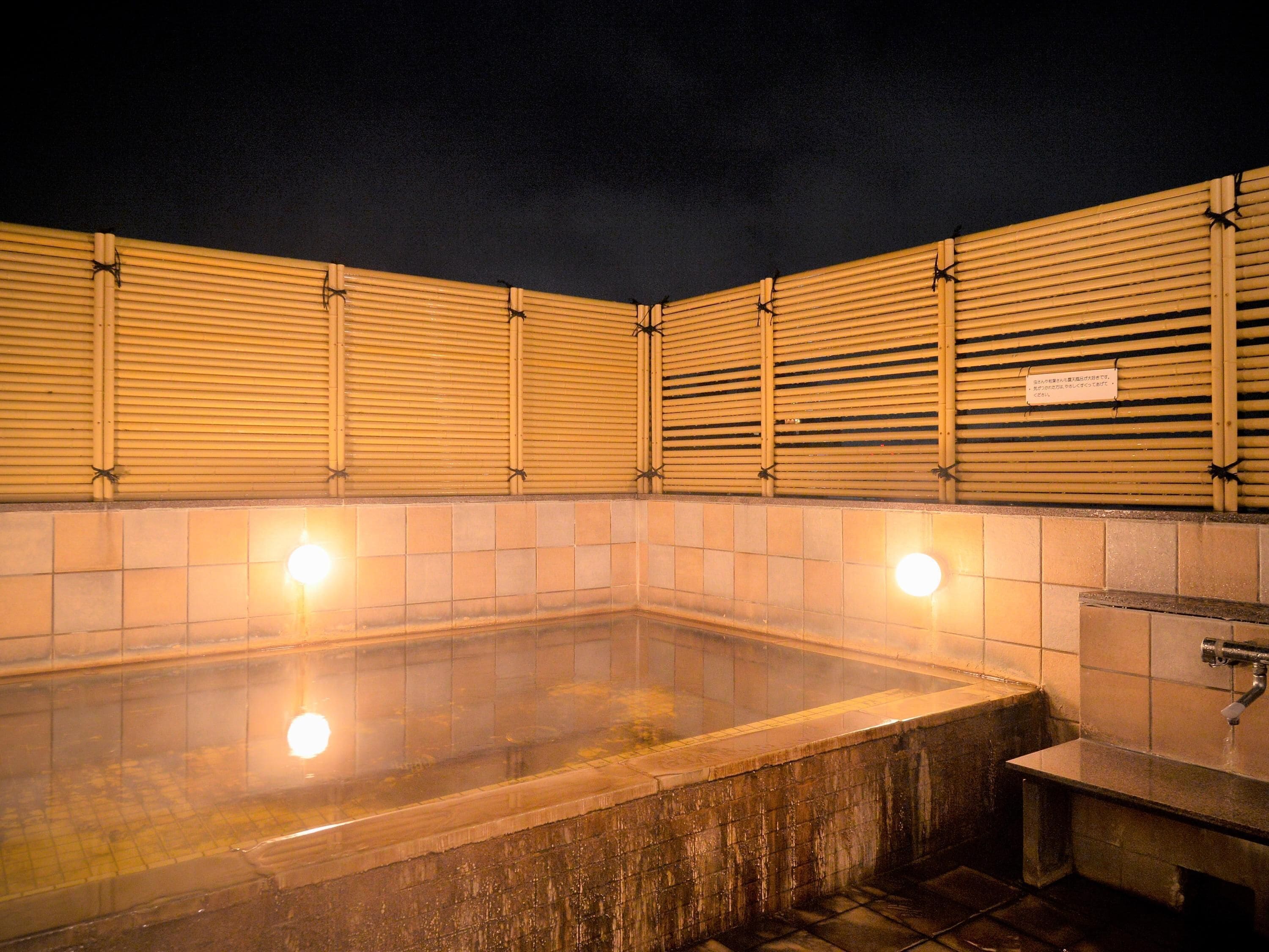 A traditional Japanese onsen with a tiled floor, wooden sliding doors, and a small bench.