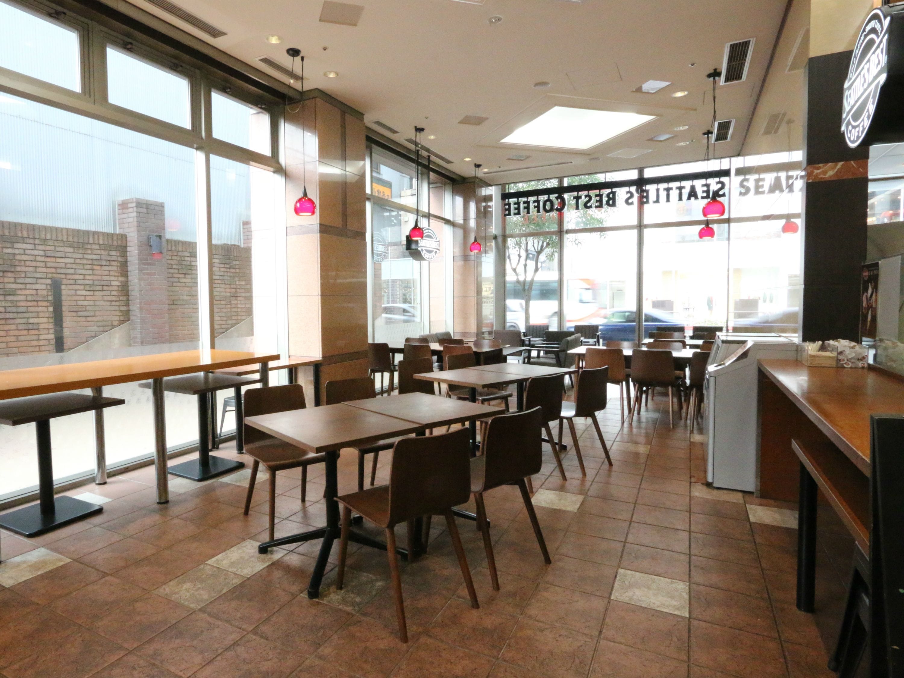 Un café avec des tables et des chaises, de grandes fenêtres et un comptoir où se trouve une machine à café.
