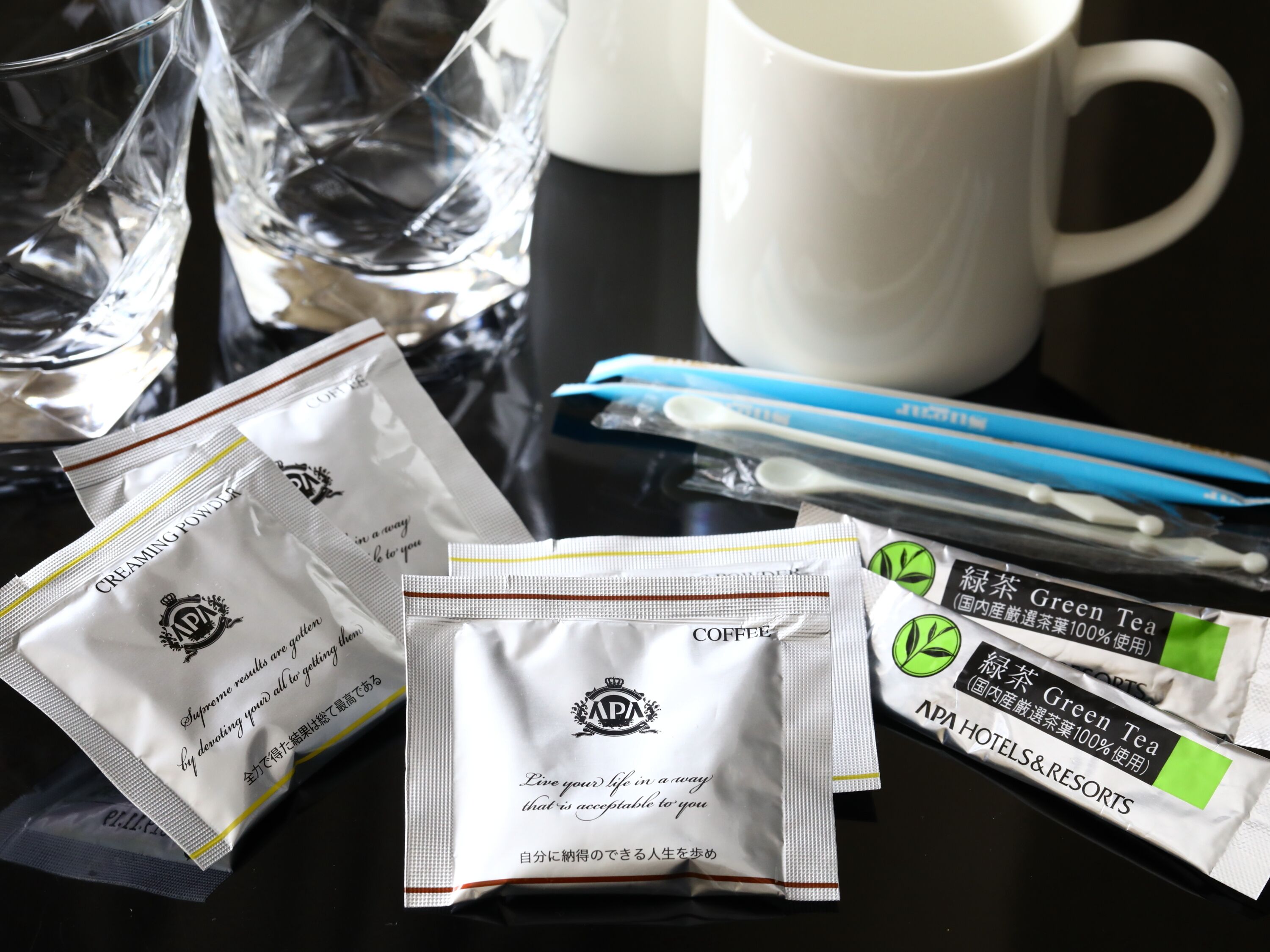 A table with various items including packets of green tea, a white mug, and a glass.