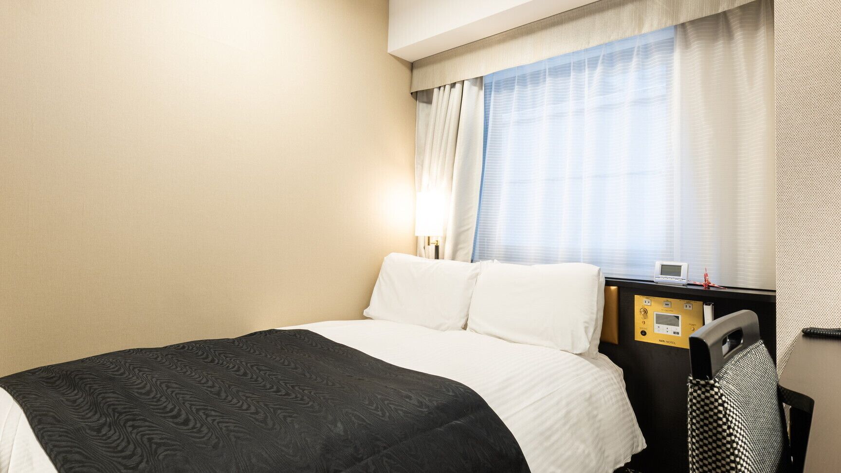 Ein Hotelzimmer mit Bett, Schreibtisch mit Bedienfeld und Fenster mit Vorhängen.
