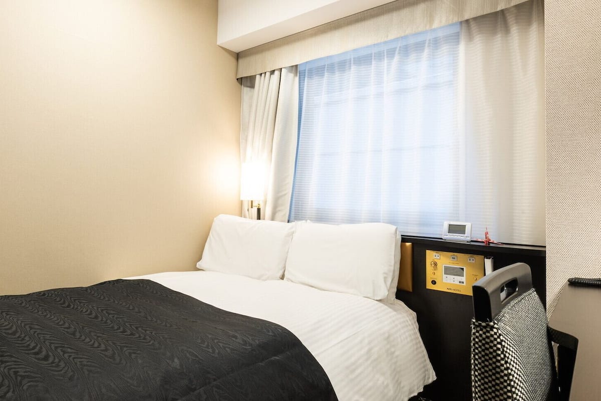 Ein Hotelzimmer mit Bett, Schreibtisch mit Bedienfeld und Fenster mit Vorhängen.