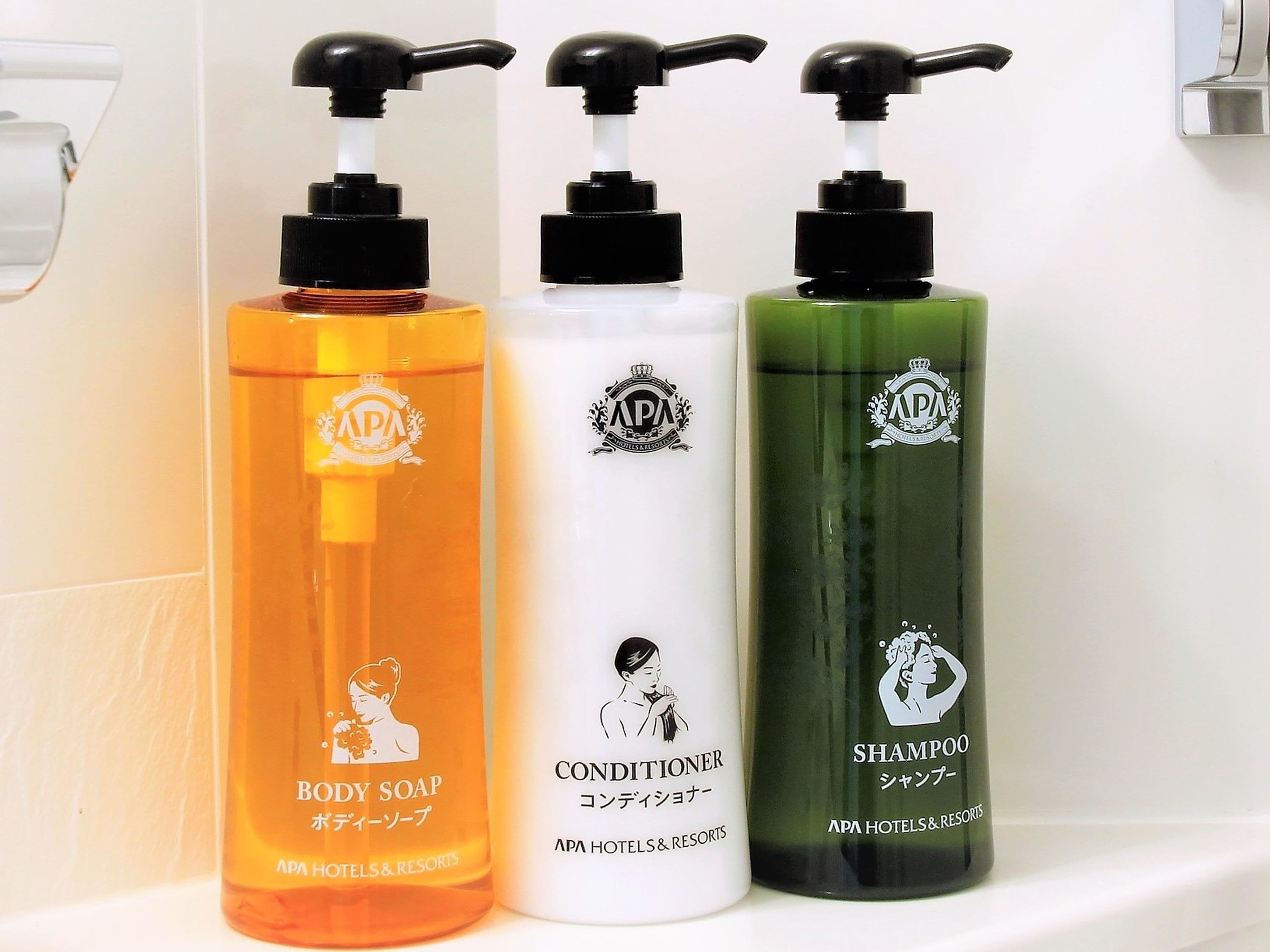 Drei Flaschen Duschseife, Conditioner und Shampoo auf einem weißen Regal.