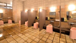 A public restroom with multiple stalls, a clock on the wall, and hand dryers.