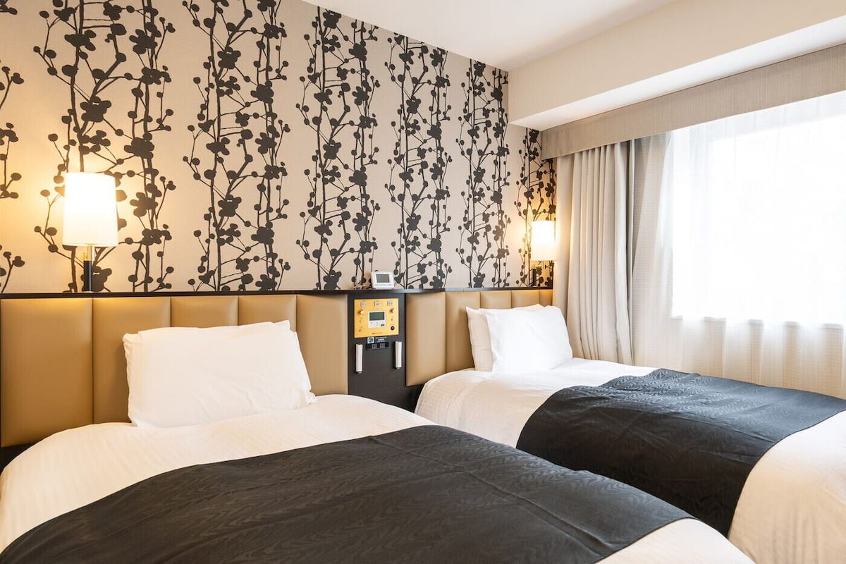 Ein Hotelzimmer mit zwei Betten, einer Steuerung und einem großen Fenster mit Vorhängen.