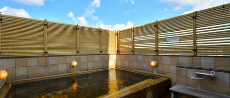 A traditional Japanese onsen with a stone bath, bamboo walls, and a tiled floor.
