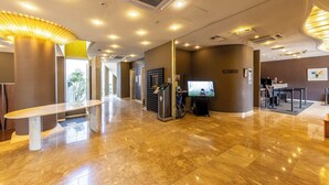 Un moderno vestíbulo de hotel con mostrador de recepción, quiosco informativo digital y espacio accesible para sillas de ruedas.