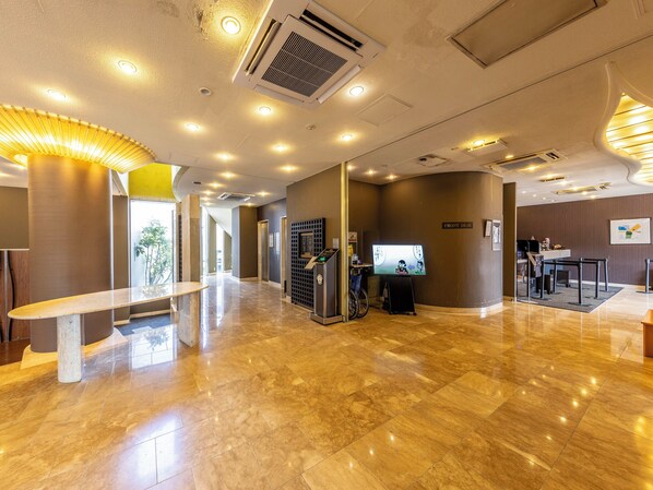 Um saguão de hotel moderno com um balcão de recepção, um quiosque de informações digital e uma área acessível para cadeiras de rodas.