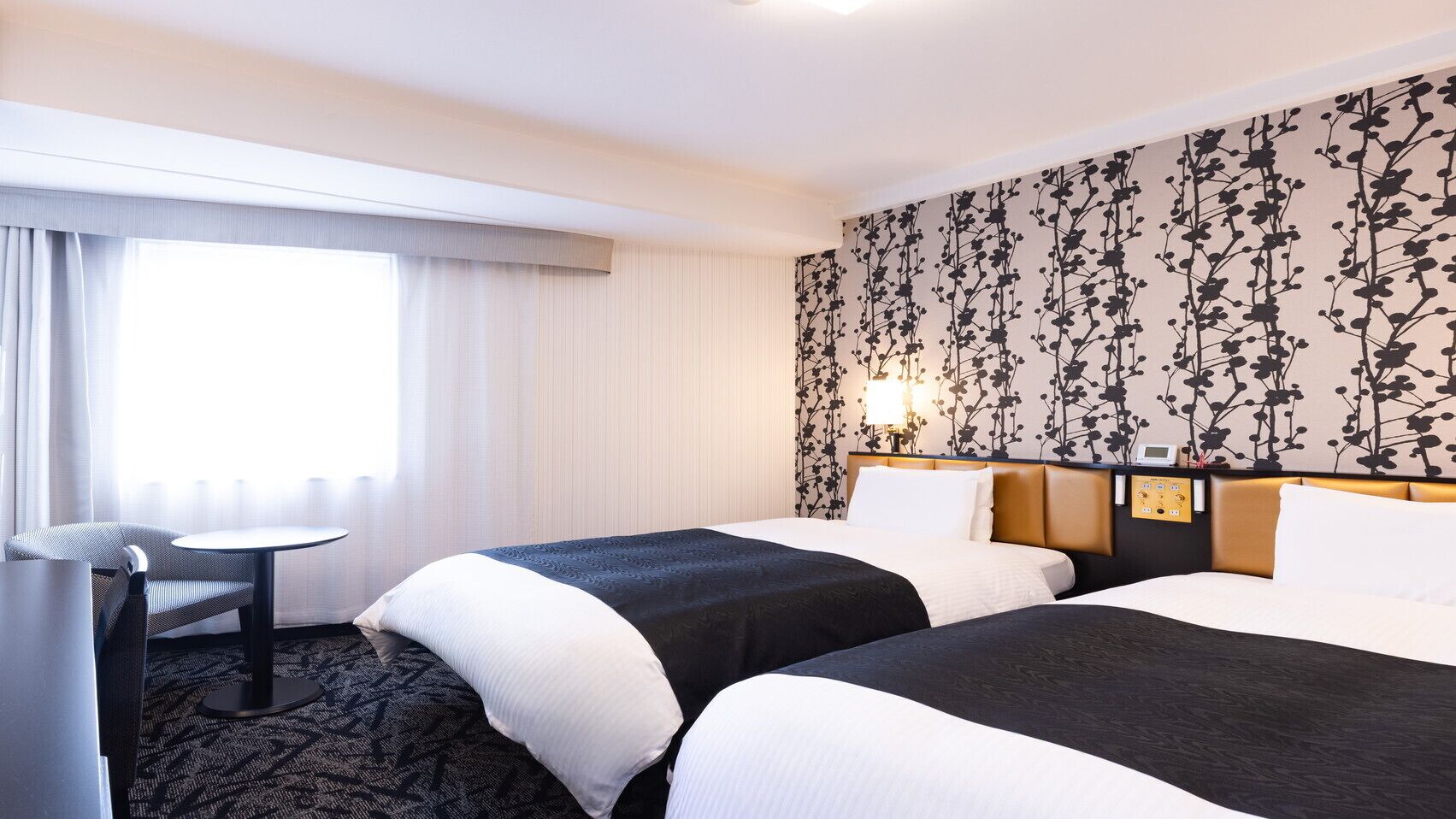A hotel room with two beds, a desk, and a window with curtains.