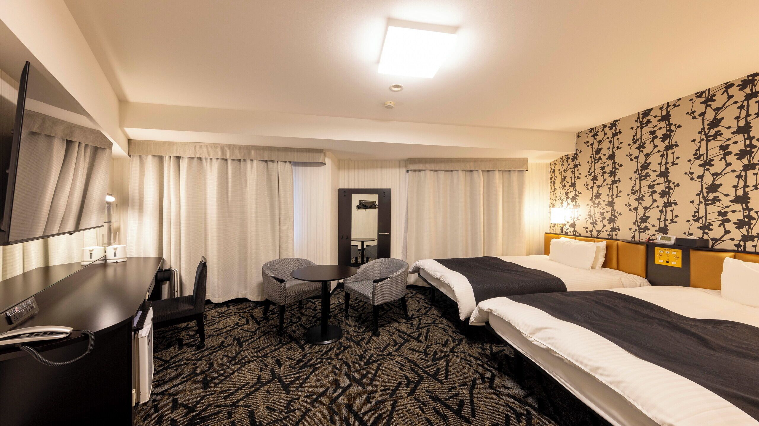 Habitación de hotel con cama, escritorio, teléfono, dos sillas, una mesita y un espejo.
