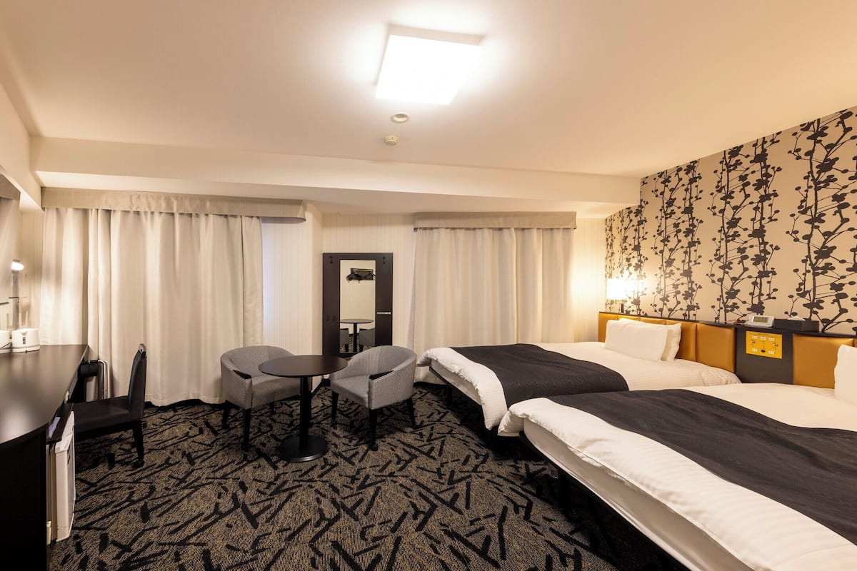 Habitación de hotel con cama, escritorio, teléfono, dos sillas, una mesita y un espejo.