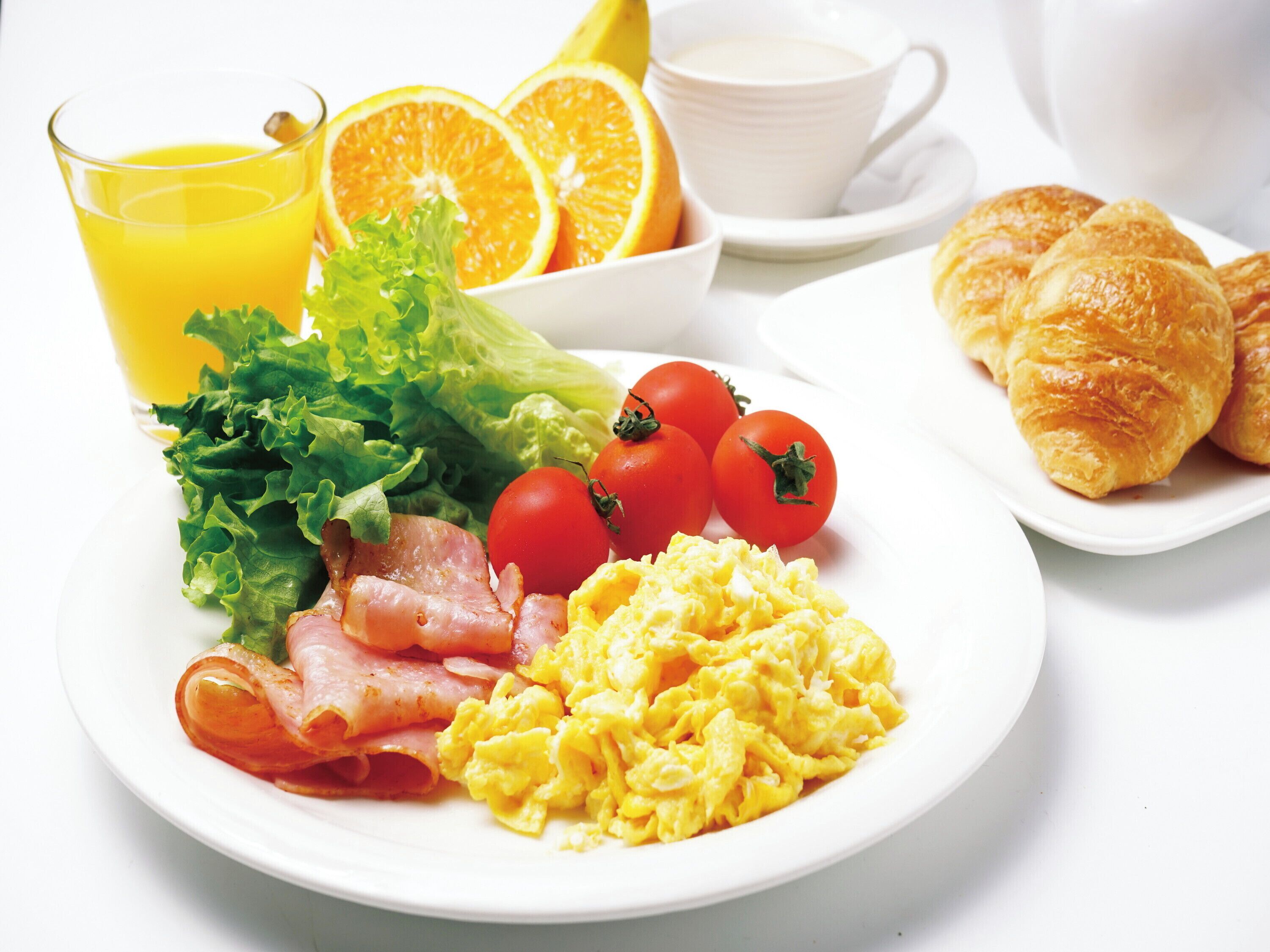 Un plato de desayuno con huevos, tocino, tomates, lechuga y gajos de naranja.