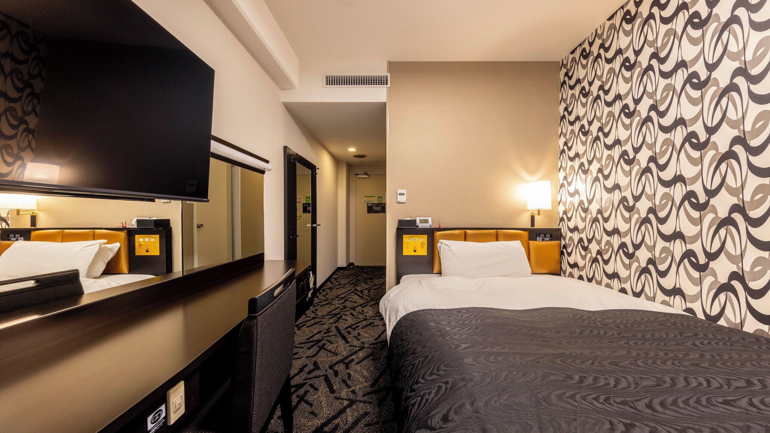 Una habitación de hotel con cama, televisión, escritorio y pared con diseño.