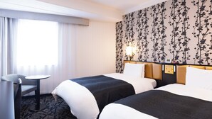 Una habitación de hotel con dos camas, un escritorio y un ventanal grande con cortinas.