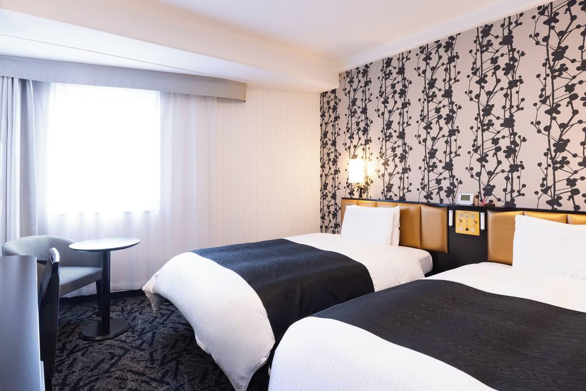 A hotel room with two beds, a desk, and a large window with curtains.