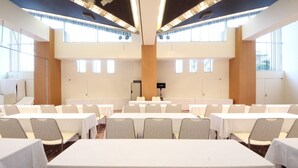 Un salón de conferencias con varias mesas y sillas, amplias ventanas y un atril central.