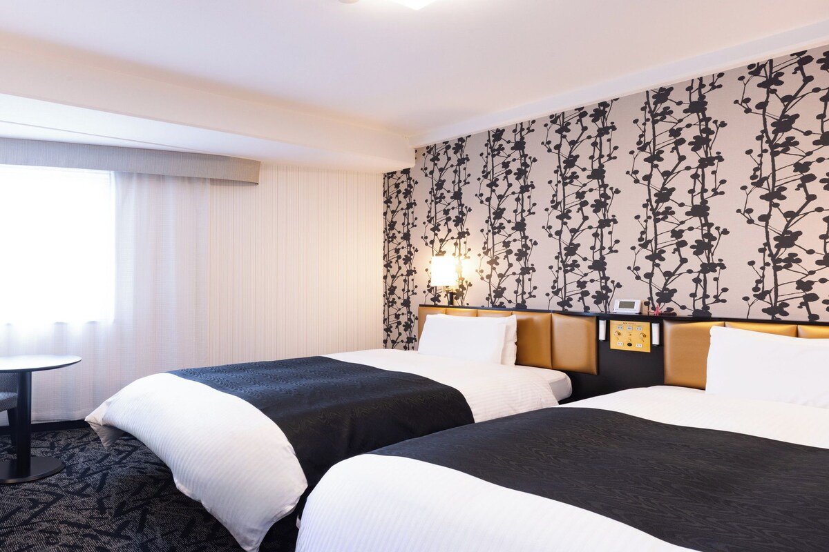 Una camera d'albergo con due letti, una scrivania e una finestra con tende.