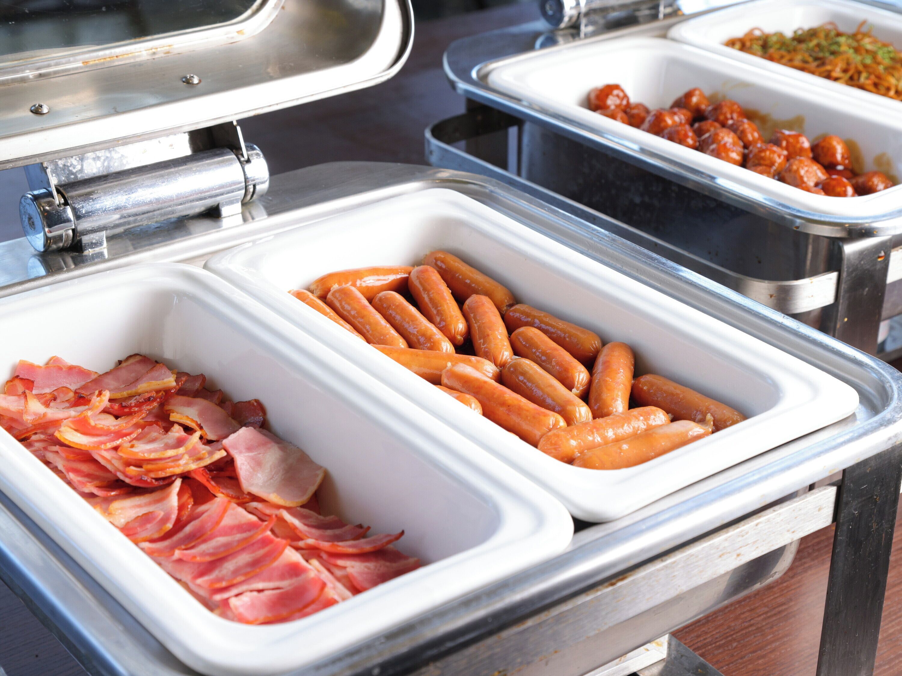 A buffet with various food items including bacon, sausages, and a dish with a sauce.