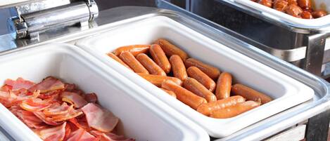 A buffet with various food items including bacon, sausages, and a dish with a sauce.