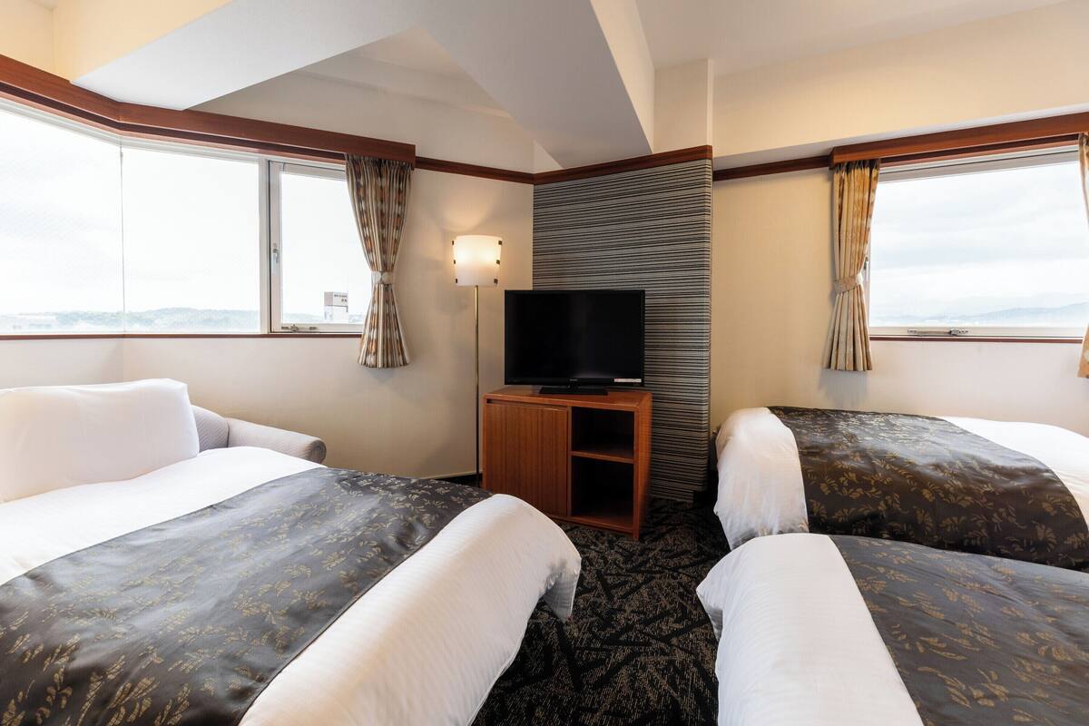 A hotel room with two beds, a TV, and a window with curtains.
