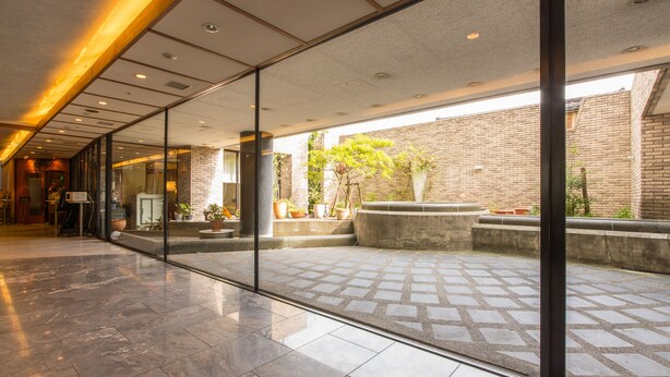 Un hall espacioso con pared de vidrio, suelo de baldosas y pared de ladrillo visible al exterior.