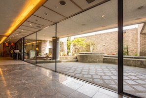 A spacious lobby with a glass wall, a tiled floor, and a brick wall visible outside. - APA Hotel Kanazawa Nomachi (Kanazawa)