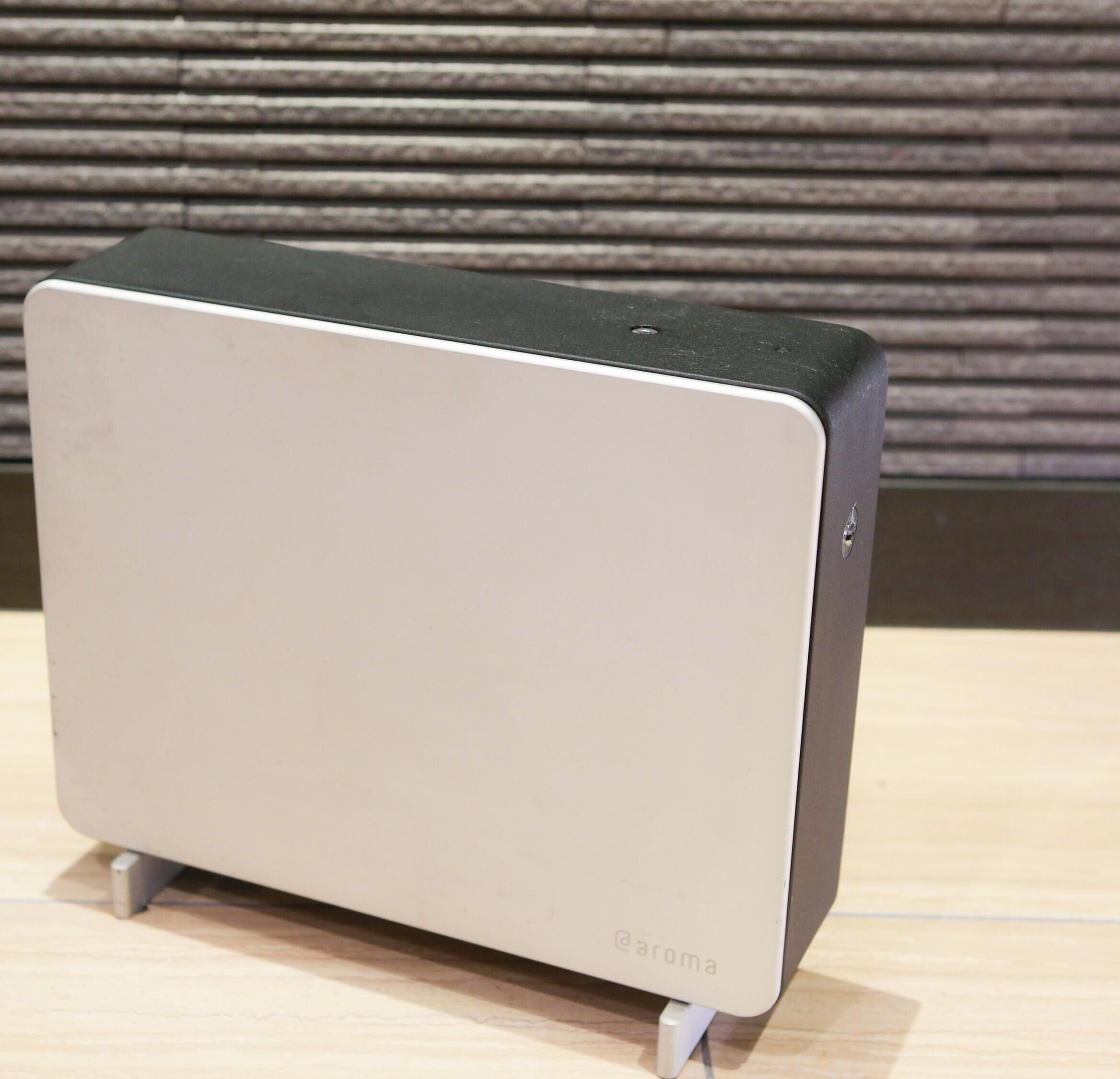 A modern, minimalist speaker with a metallic finish and a logo on the bottom.