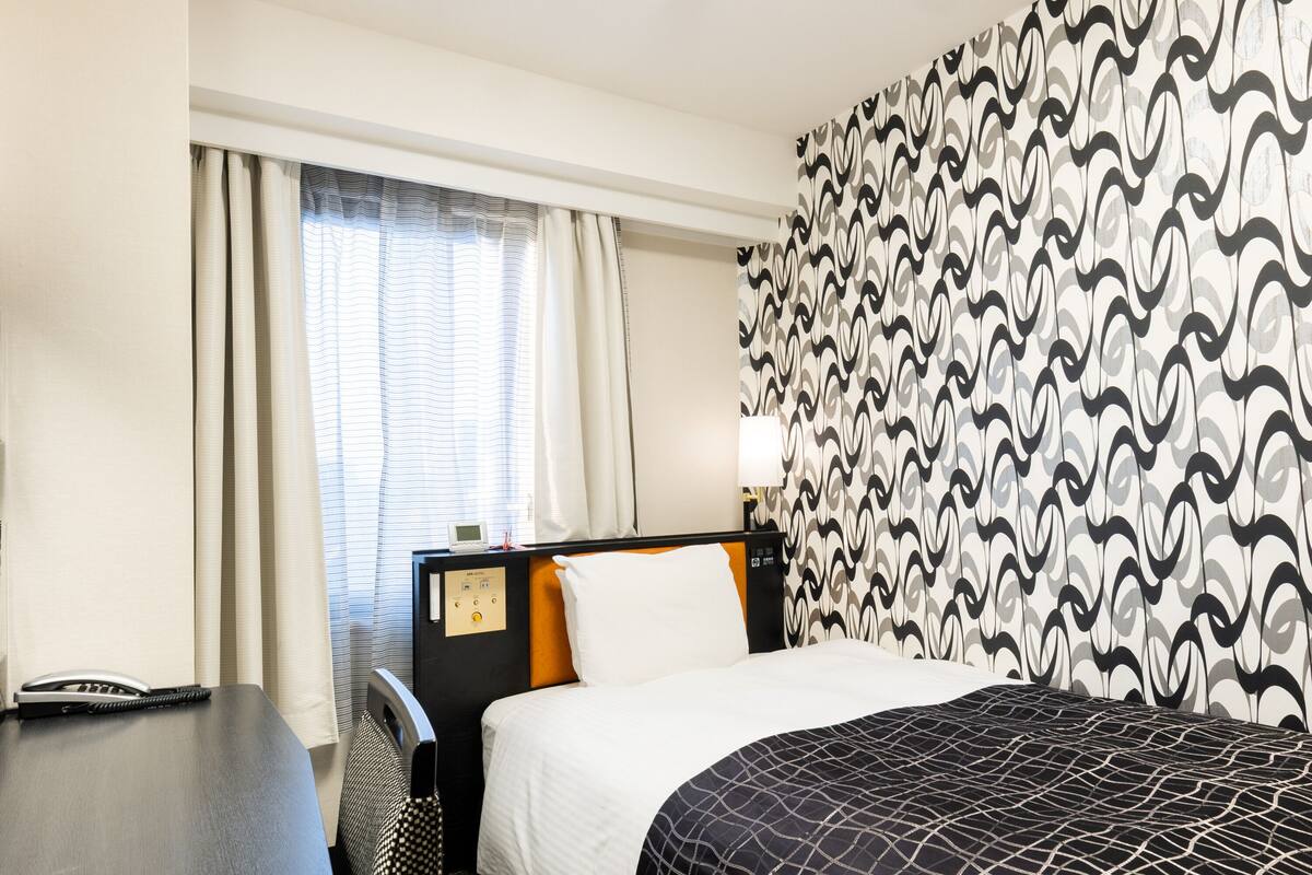Ein Hotelzimmer mit Bett, Schreibtisch, Telefon und einem Fenster mit Vorhängen.