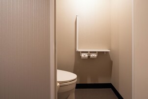 Un baño pequeño y limpio con inodoro, un estante con papel higiénico y una pared lisa.
