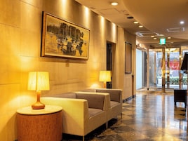 A lobby with a seating area, two lamps, a painting, and a door with an exit sign.