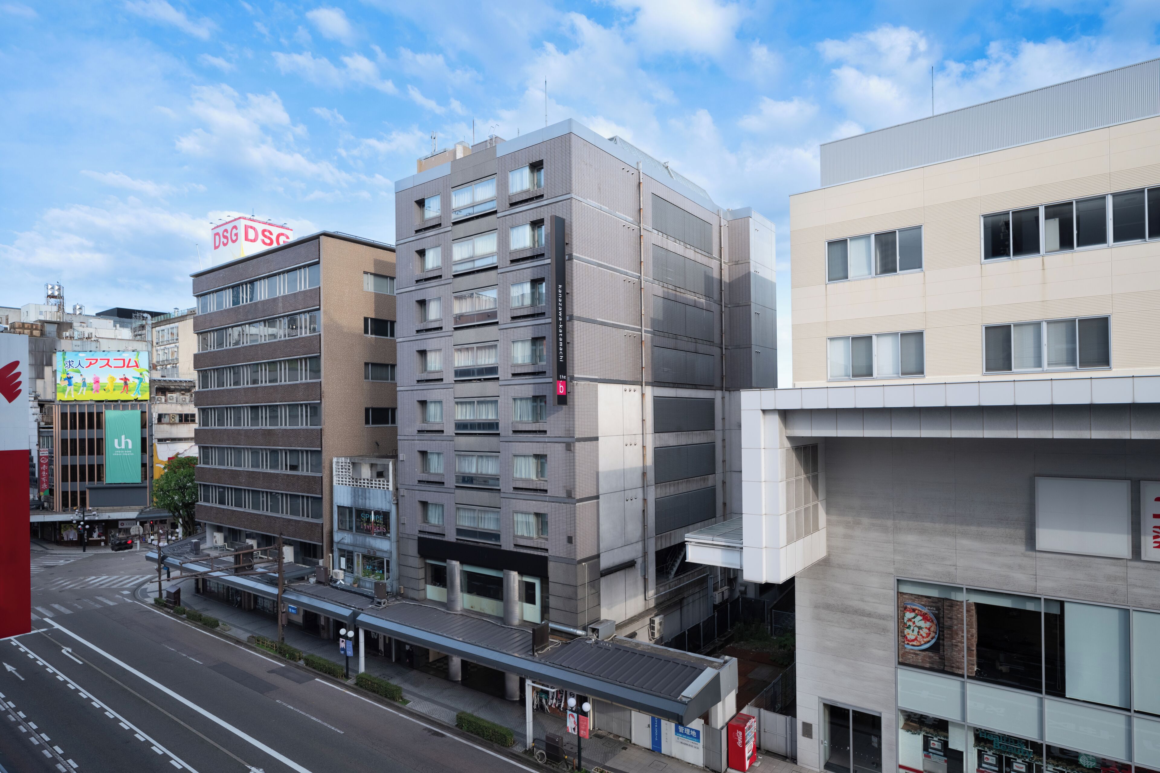 A multi-story building with a modern architectural design, featuring a mix of glass and metal facades, and a pedestrian overpass.