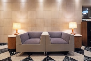 A lobby with two sofas, a marble floor, and lamps on either side.