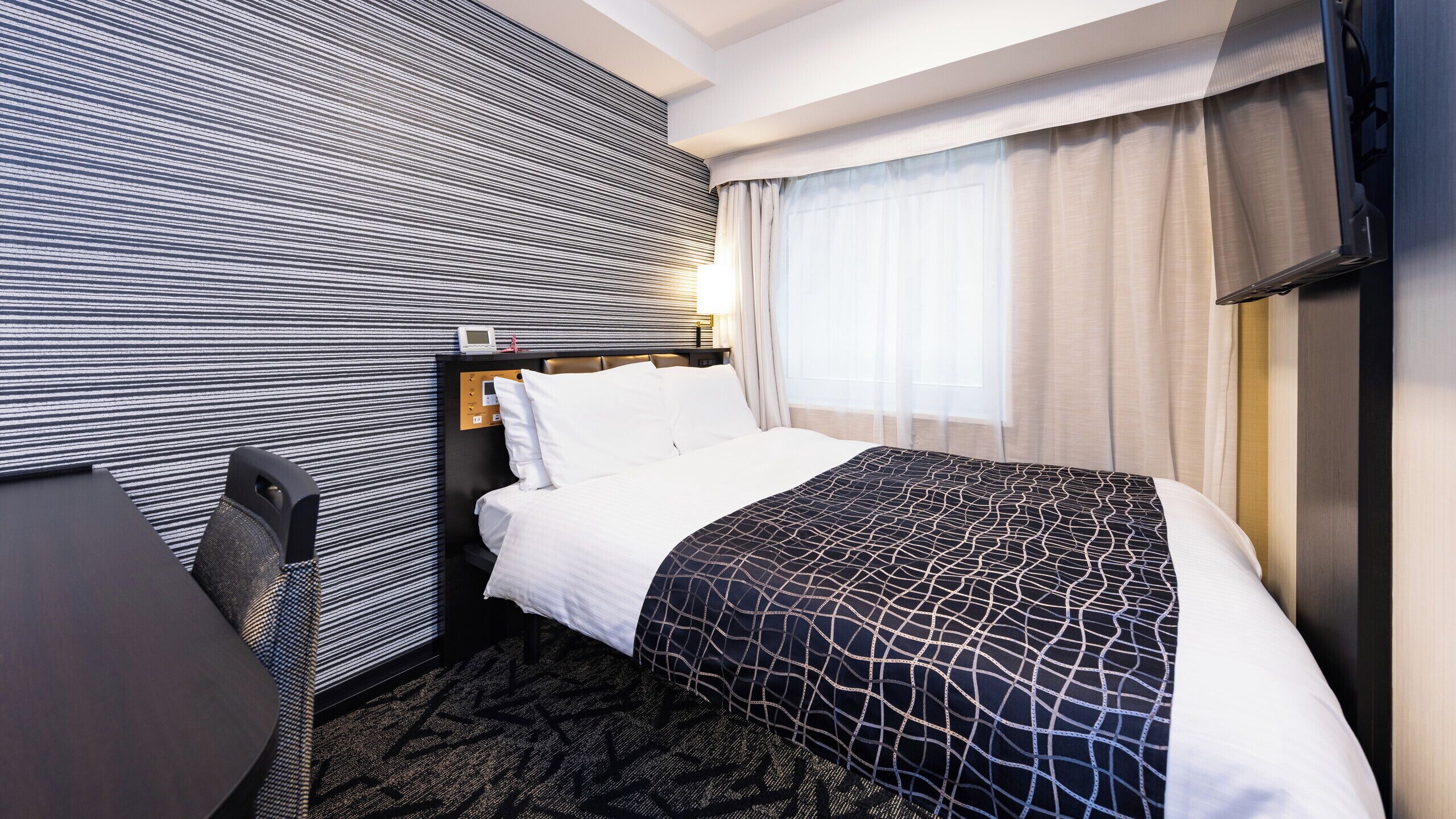Une chambre d’hôtel équipée d’un lit, d’un bureau, d’une chaise, d’un panneau de commande et d’un téléviseur.