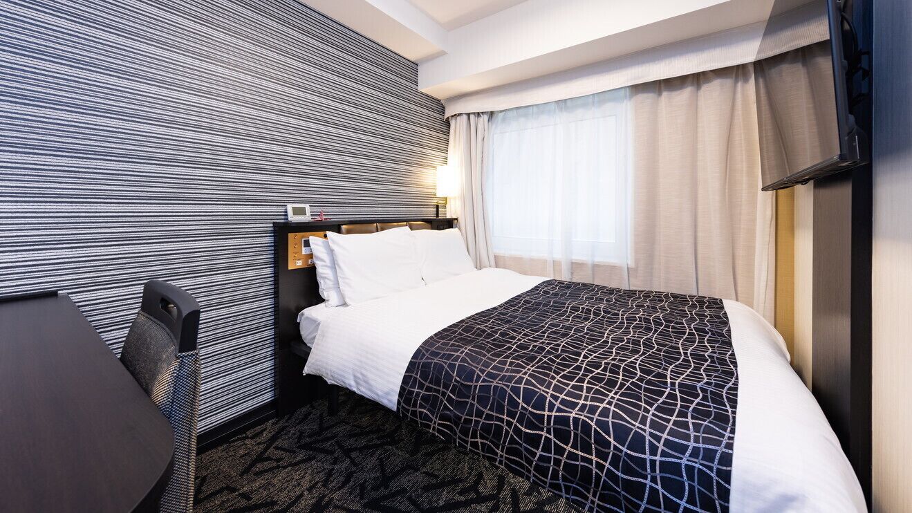 Une chambre d’hôtel équipée d’un lit, d’un bureau, d’une chaise, d’une télévision et d’une fenêtre avec des rideaux.