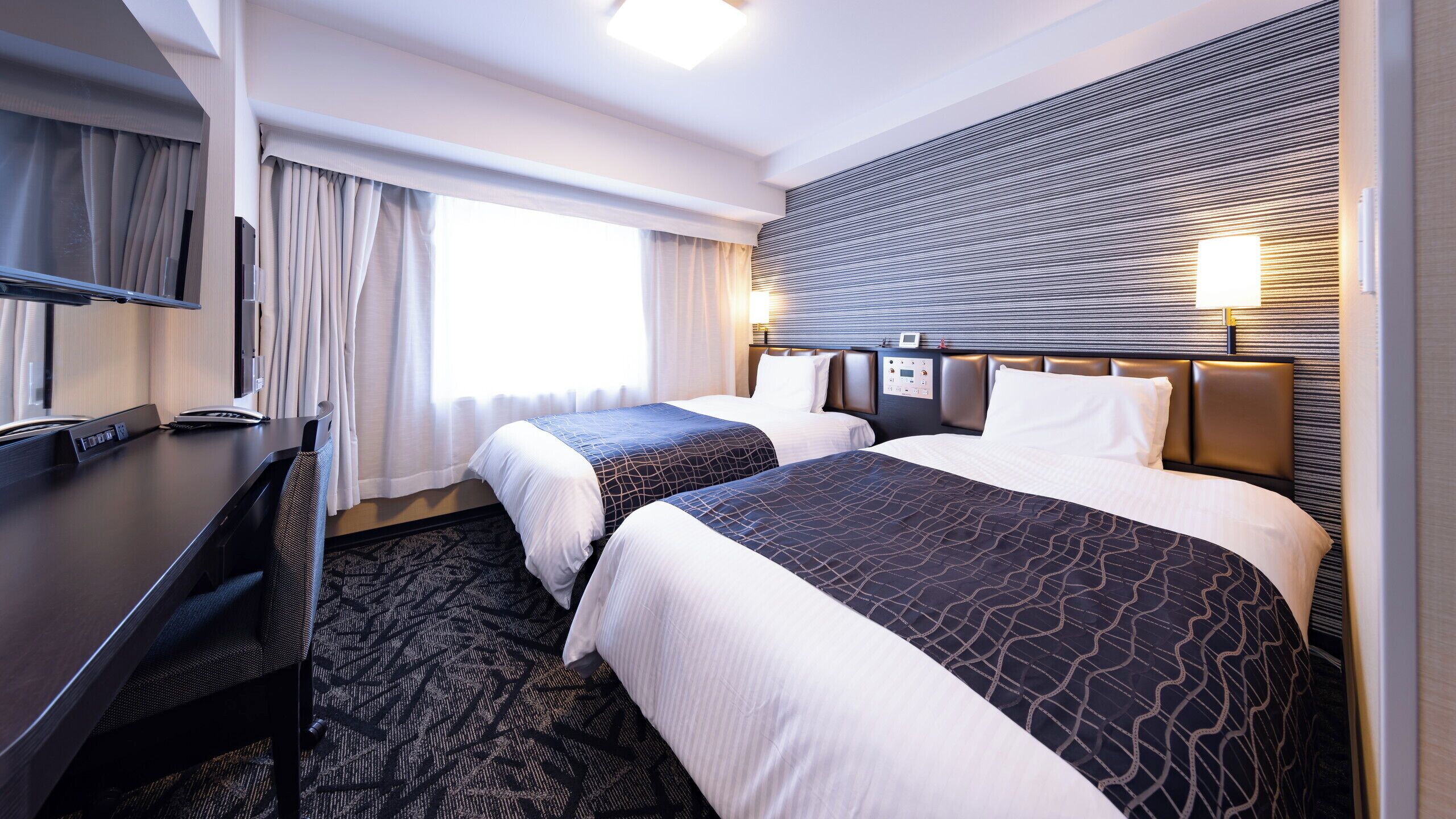 Une chambre d’hôtel avec deux lits, un bureau, une télévision et un panneau de commande.
