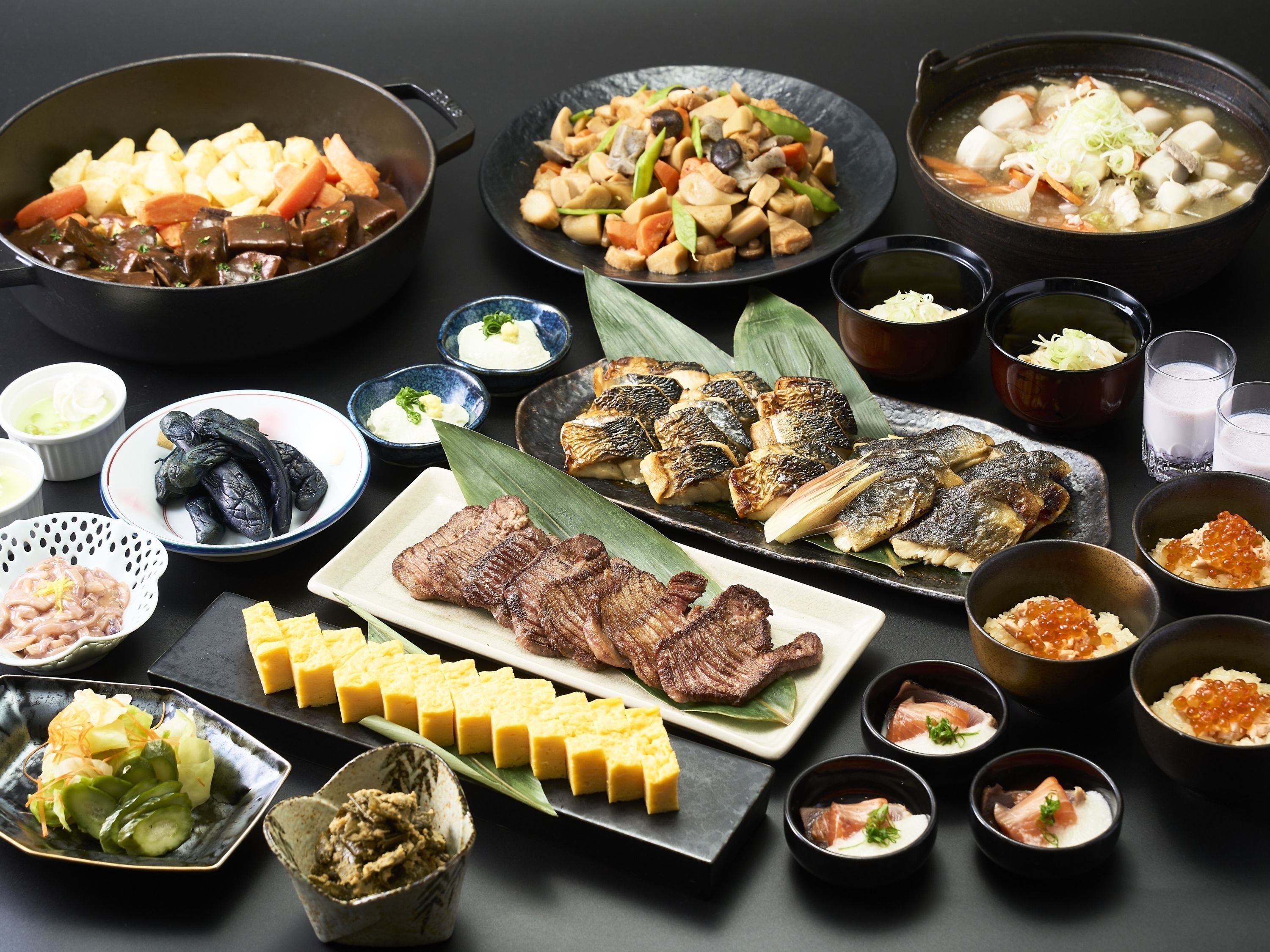 Diversos pratos japoneses, incluindo carne grelhada, peixe e legumes, dispostos sobre uma mesa preta.