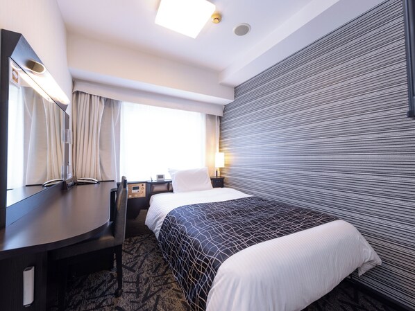 Une chambre d’hôtel comprenant un lit, un bureau, une chaise, un grand miroir, une fenêtre avec des rideaux et un mur à motifs.