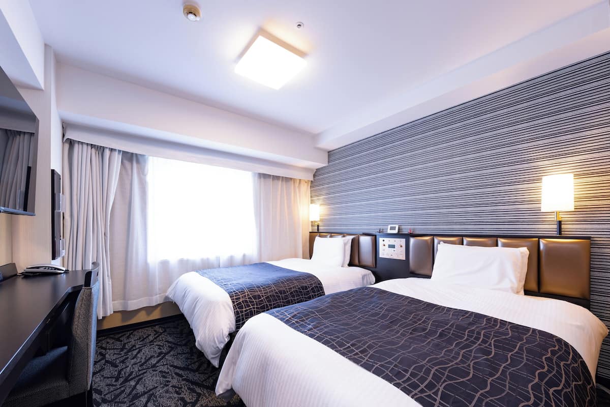 A hotel room with two beds, a desk, a chair, a TV, and a window with curtains.