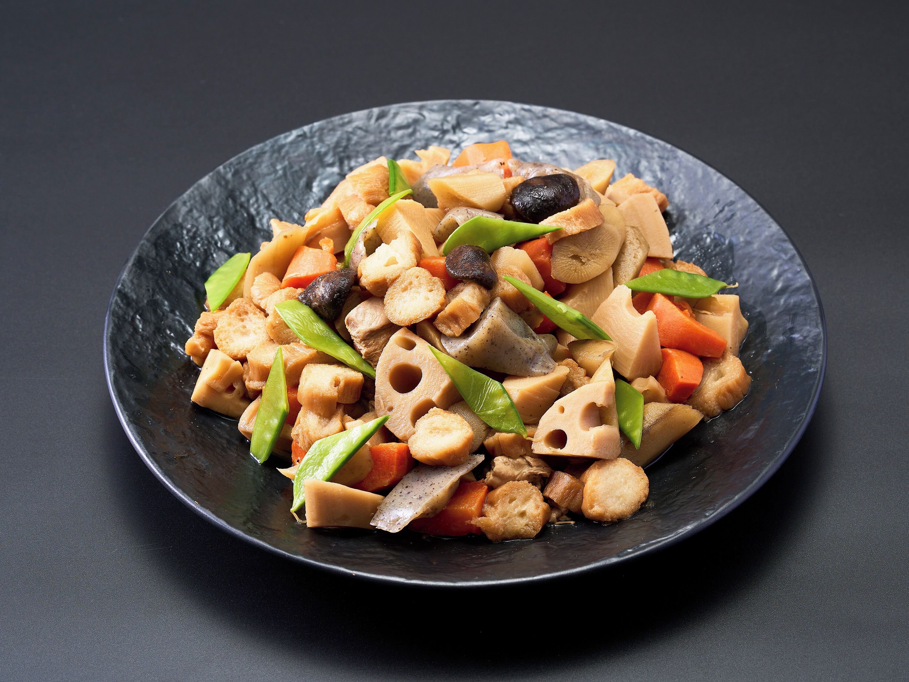 A dish with various vegetables and tofu on a dark plate.